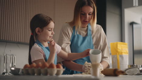 cute-little-daughter-is-helping-to-her-mother-in-kitchen-pouring-water-on-dough-woman-is-kneading-by-hands
